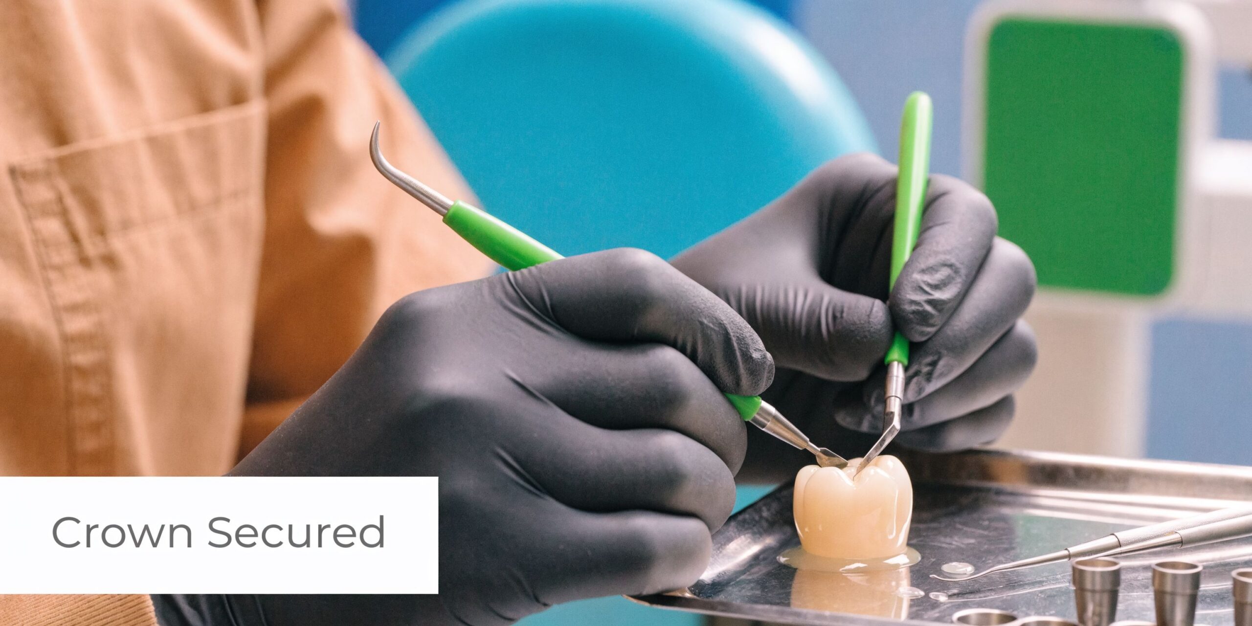 A dental professional in black gloves uses precision tools to handle a dental crown on a tray.