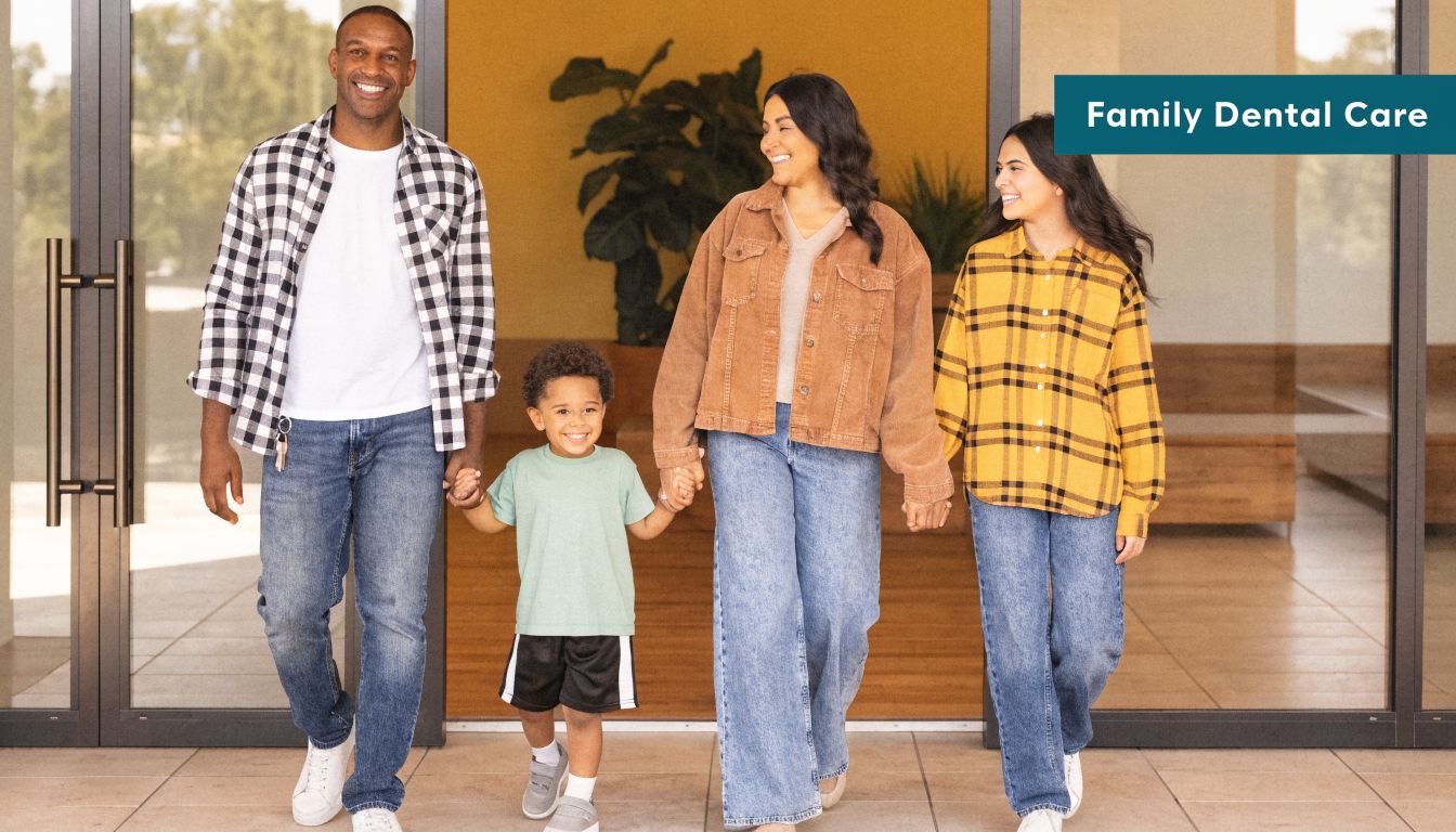 A happy family of four walking out of a modern dental clinic entrance holding hands together.