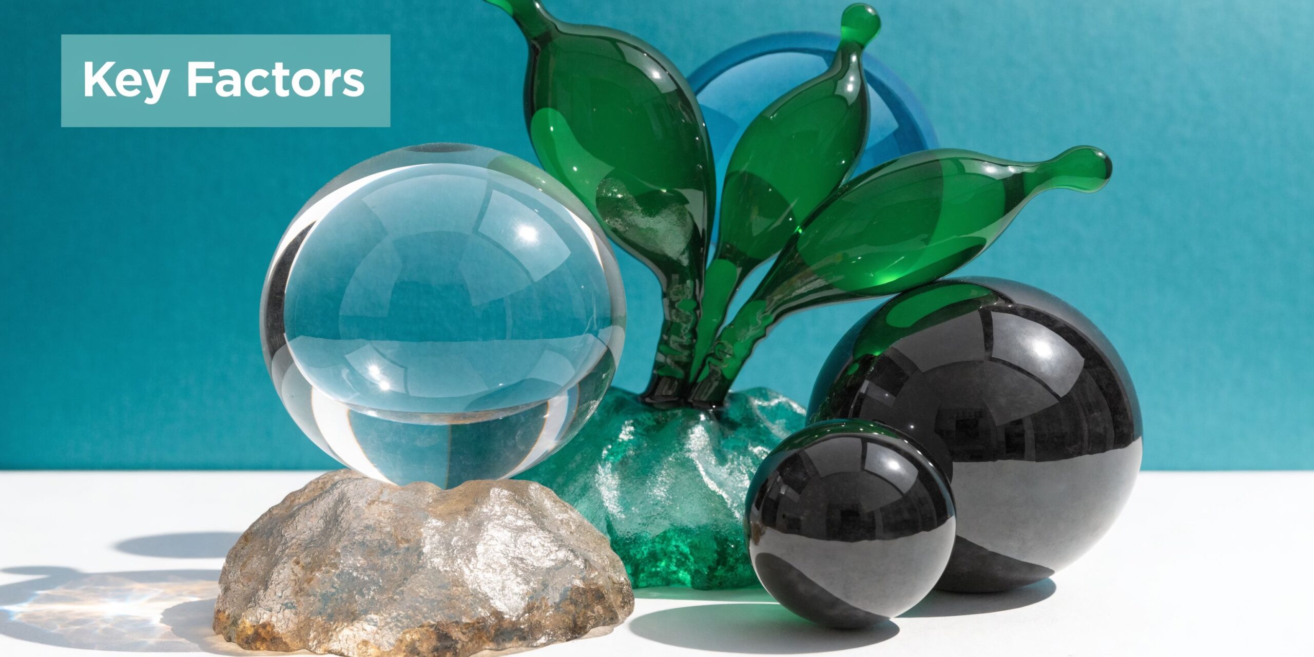 A clear glass sphere, black spheres, and green glass leaves displayed on a textured stone base.