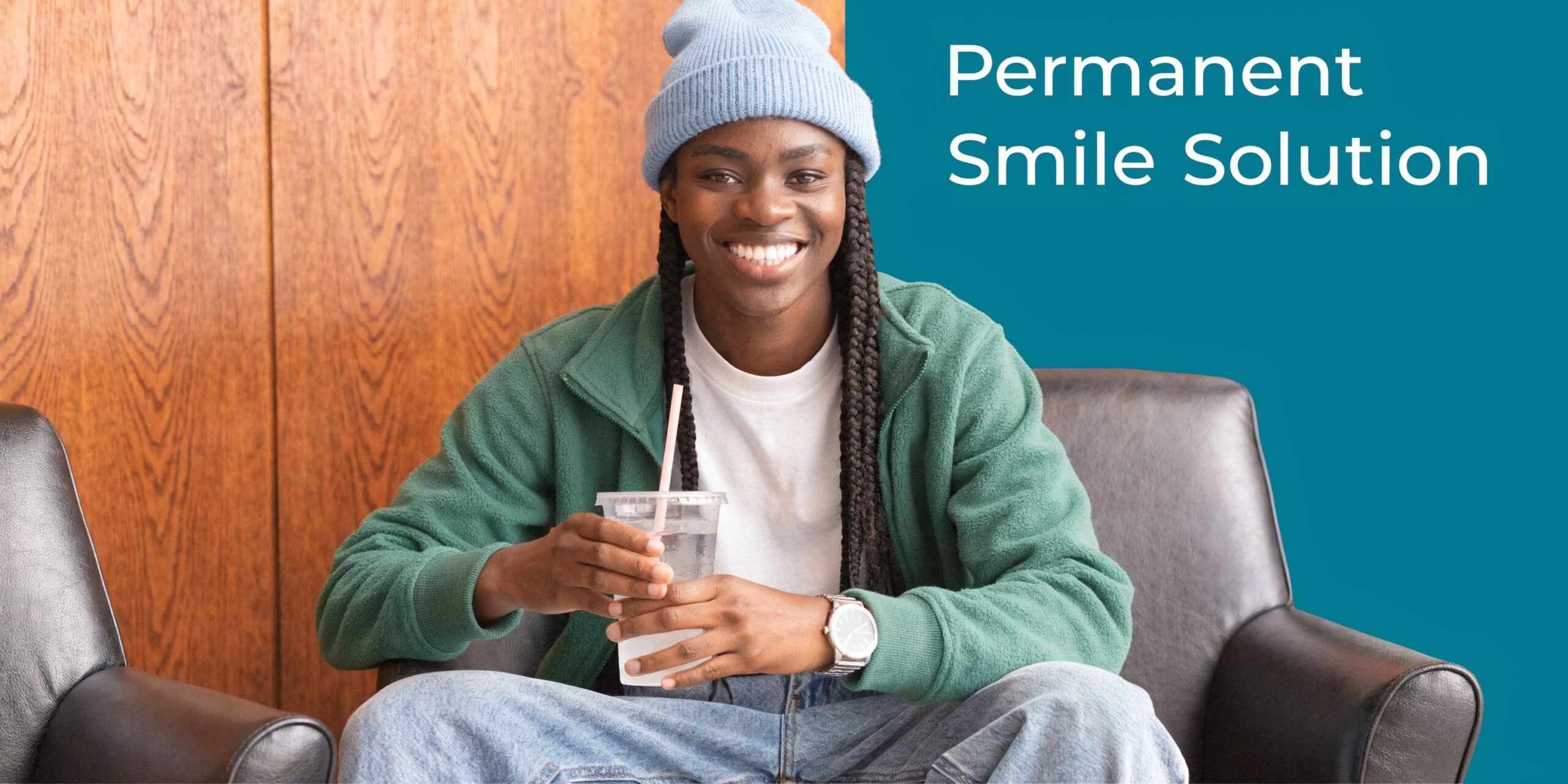 A smiling young person wearing a blue beanie and green sweater holding a plastic cup with a straw.