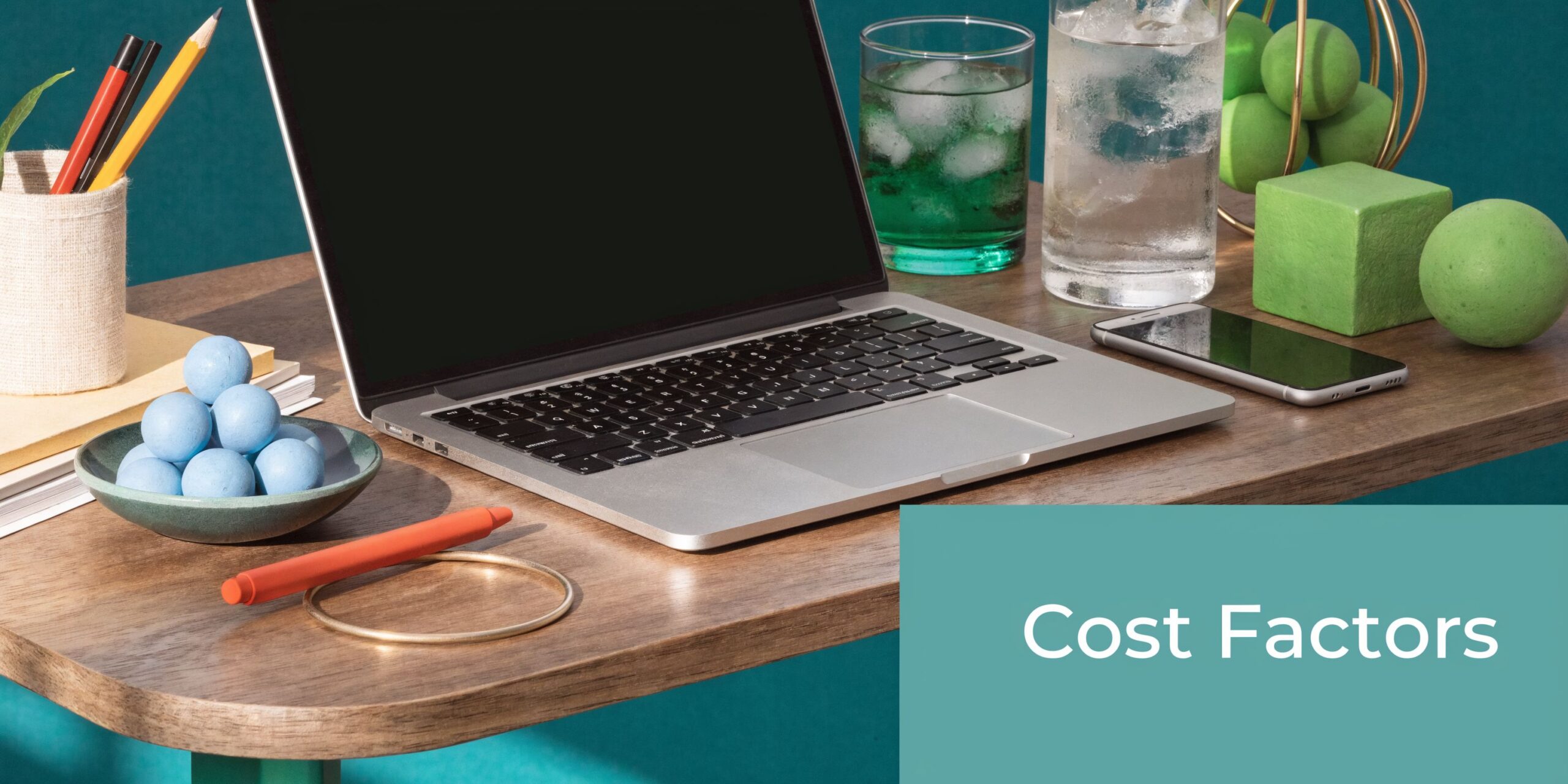 A modern workspace featuring a laptop, smartphone, drinking glasses, and decorative green and blue geometric objects.