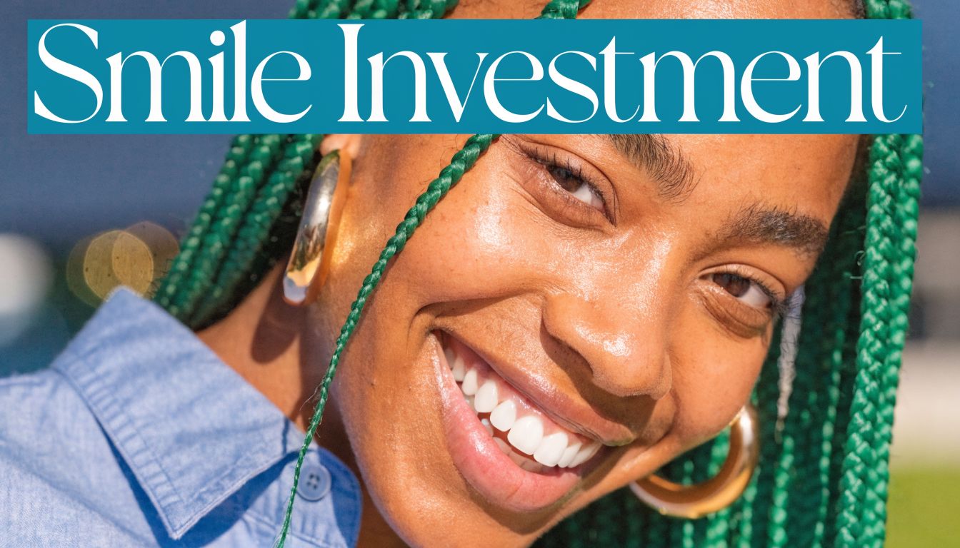 A close-up of a smiling young woman with green braided hair and gold hoop earrings.