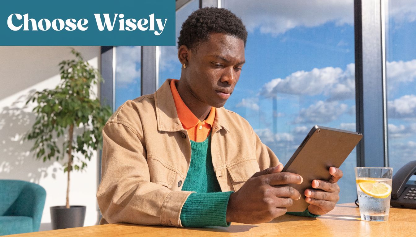 A young man sitting at an office desk looking focused at his tablet device in a workspace.