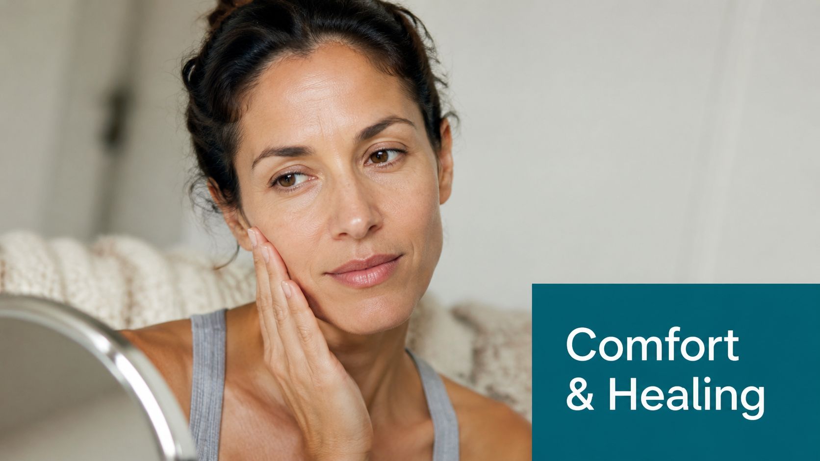 A woman gently touching her cheek while looking into a small mirror, reflecting comfort and healing.